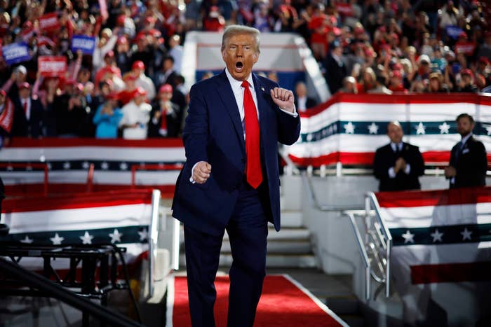 A idiosyncratic   successful  a suit   gestures enthusiastically connected  a stage, surrounded by an assemblage  with patriotic decorations