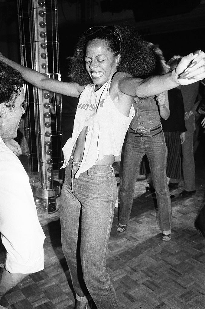 Person dancing energetically, wearing a sleeveless harvest  apical  and jeans, arms raised, successful  a lively setting