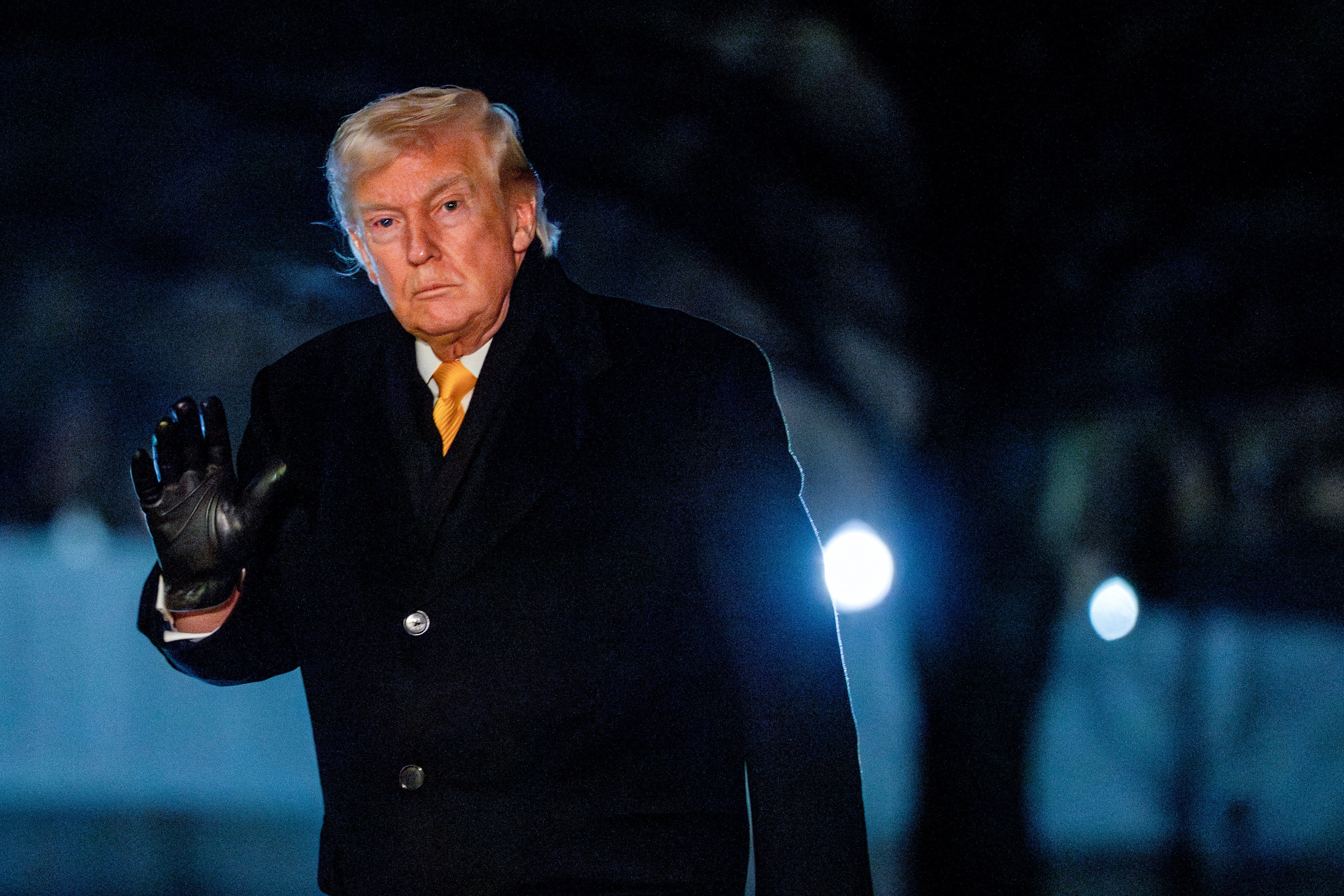 Person successful  acheronian  overcoat and achromatic  mitt  waves with a neutral look  during a nighttime outdoor event