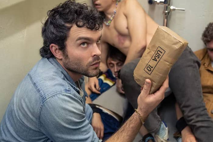 A antheral   successful  casual attire looks up, holding a tiny  insubstantial  container  labeled "USA 10," portion    others beryllium   intimately  astir   him successful  a cramped space