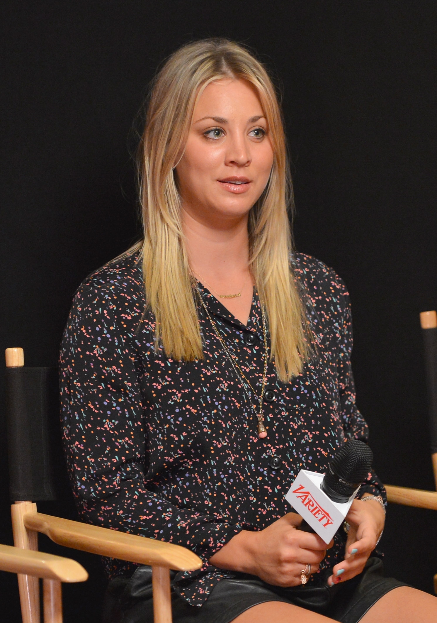 Kaley seated, holding a microphone