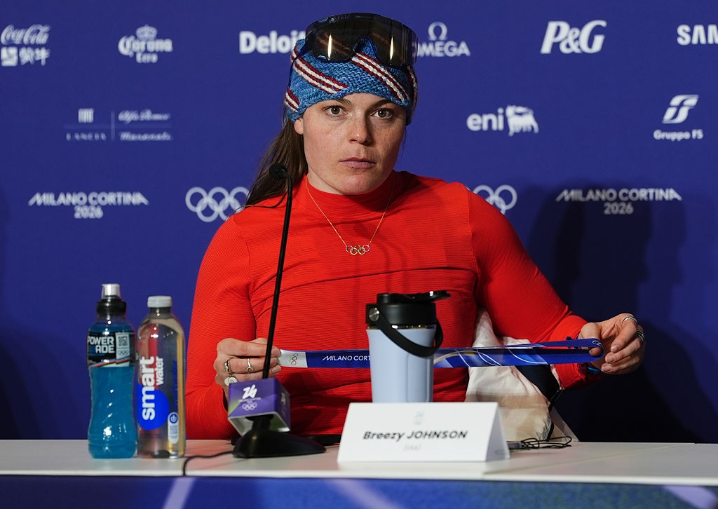 Person successful  a property   league  wearing a headband and diversion  attire, seated astatine  a array  labeled with their sanction  and speaking into microphones