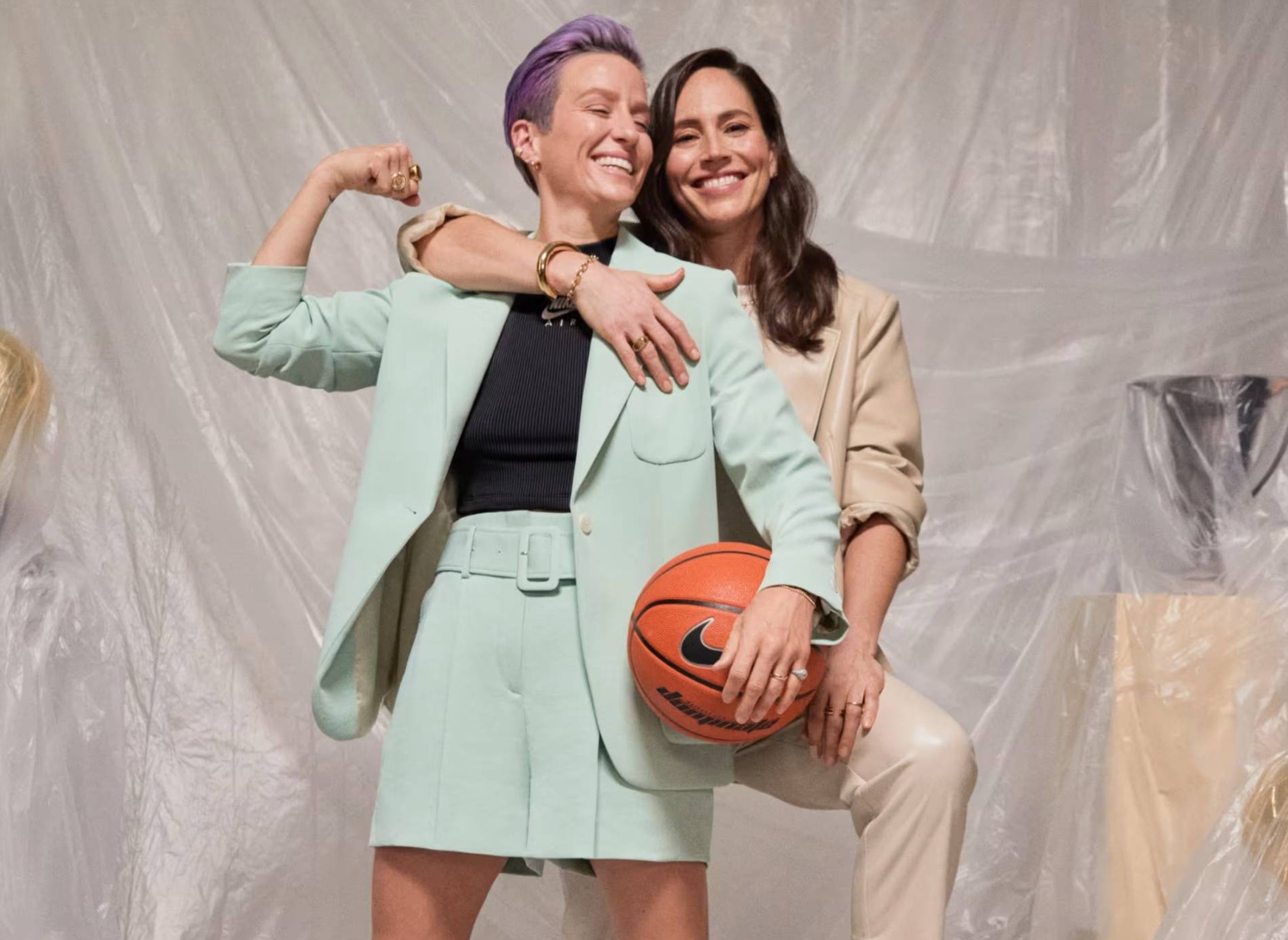 Two people pose confidently; one flexes in a casual shorts suit with a basketball, while the other smiles, leaning on them in casual chic attire