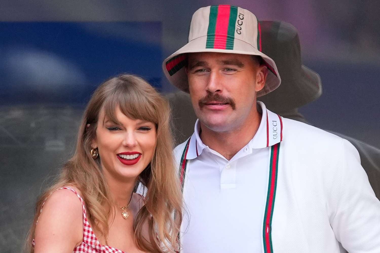 I don't know who they are. A smiling woman in a gingham dress stands next to a man in a bucket hat and white jacket with sporty accents