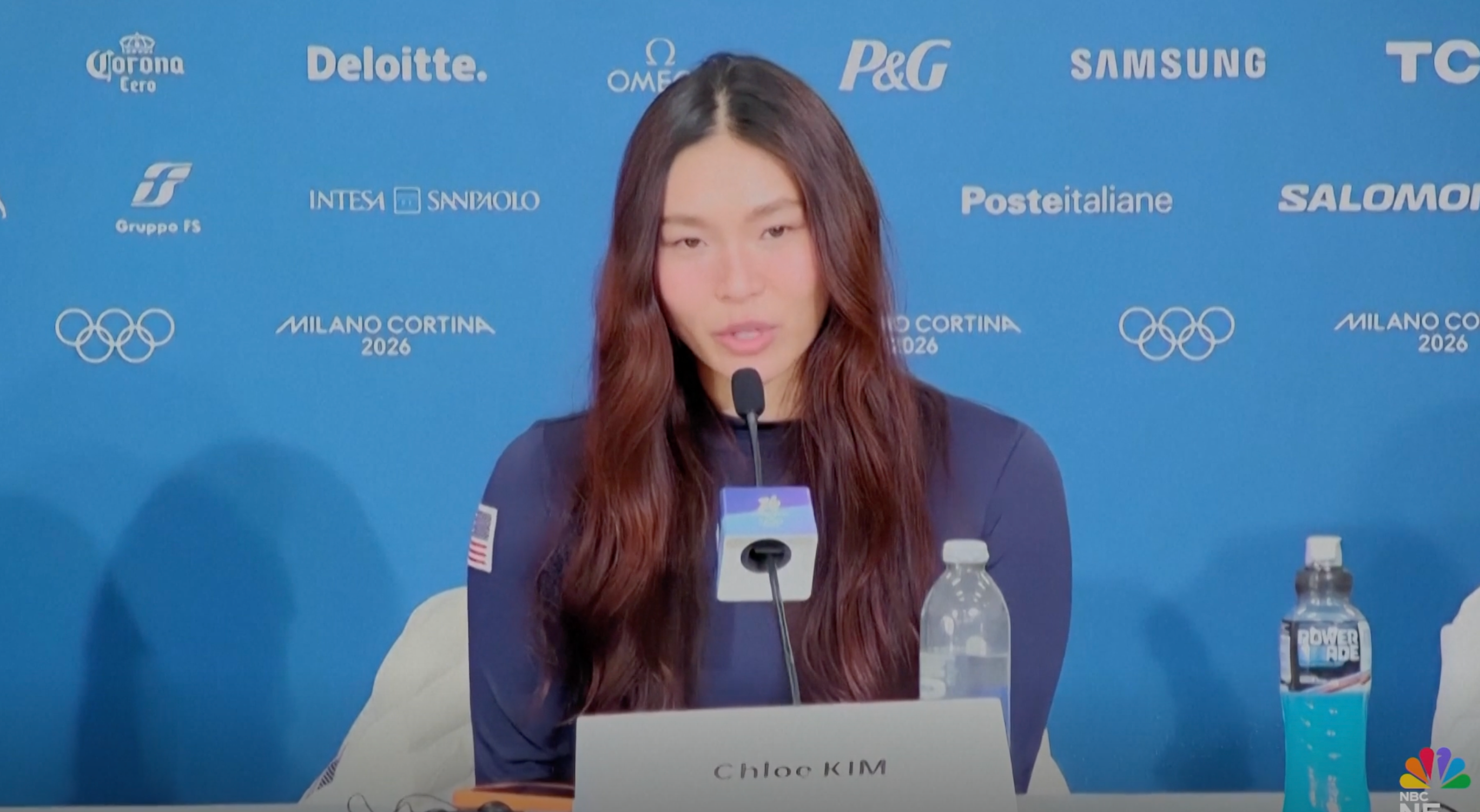 Person astatine  a property   conference, seated astatine  a array  with microphones. The Olympic rings and sponsor logos are disposable   successful  the background