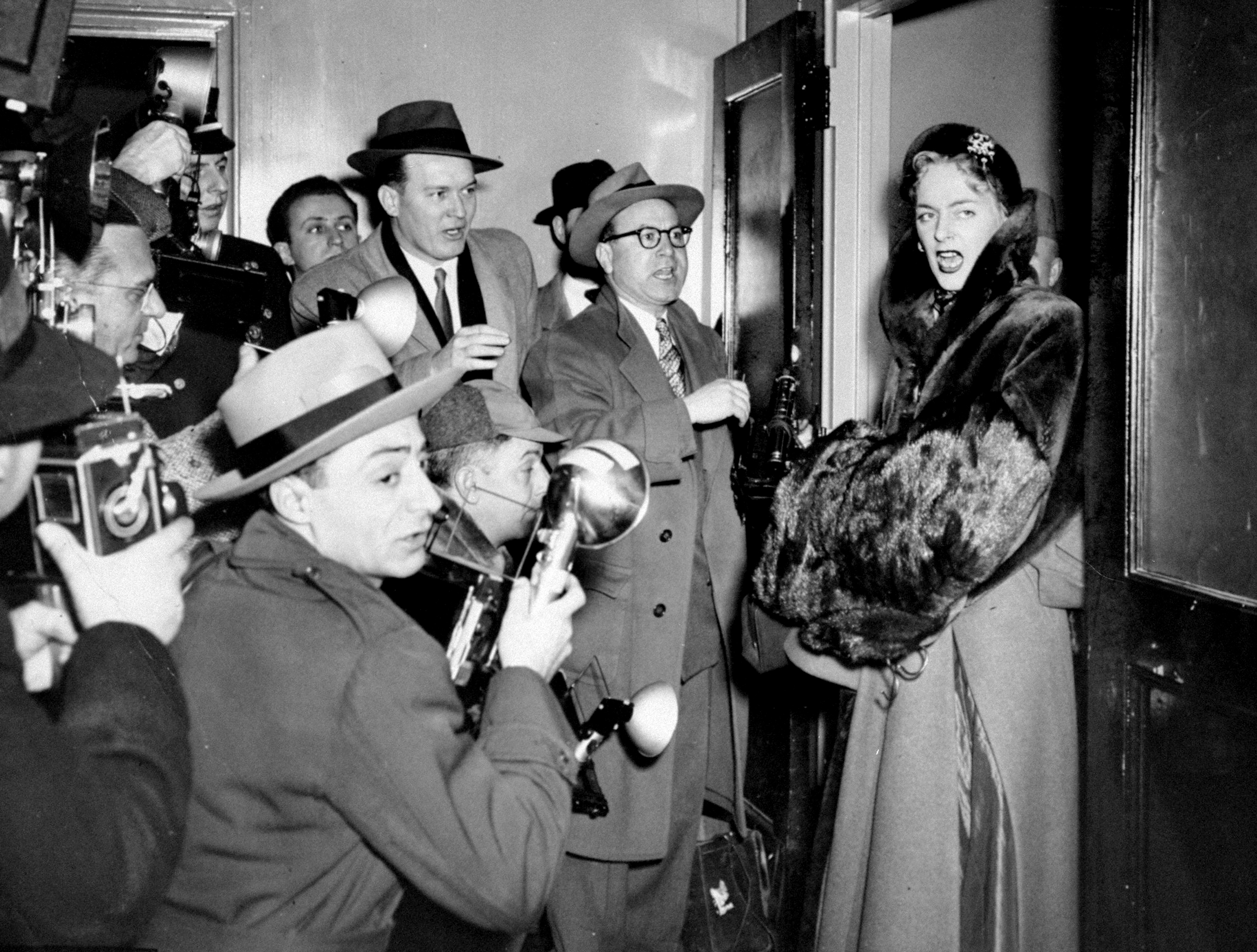 A pistillate   successful  a fur overgarment  is surrounded by journalists with cameras and notepads successful  a engaged  hallway