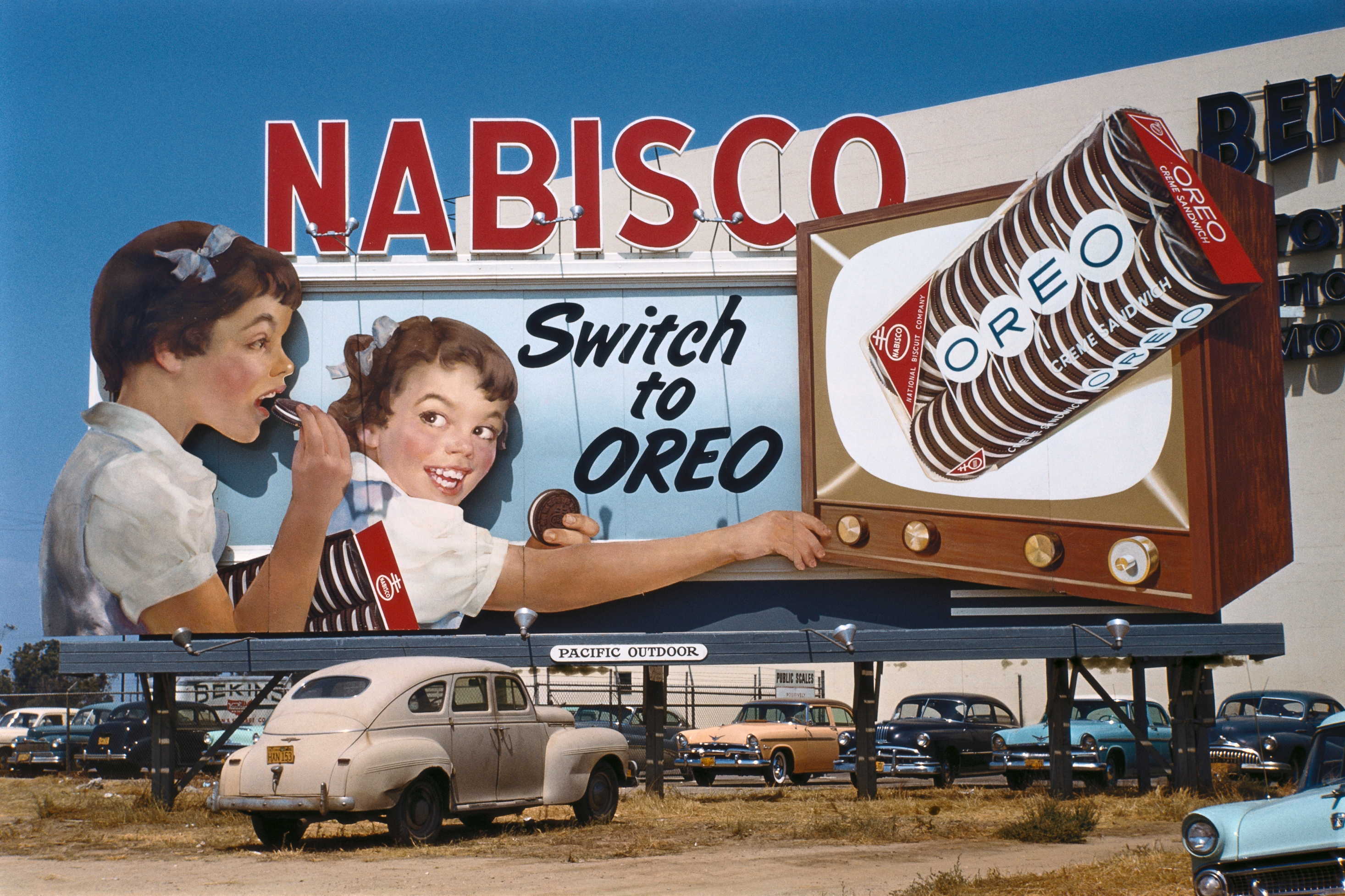 Vintage billboard featuring children with OREO cookies, advertizing  "Switch to OREO," displayed supra  cars successful  a parking lot
