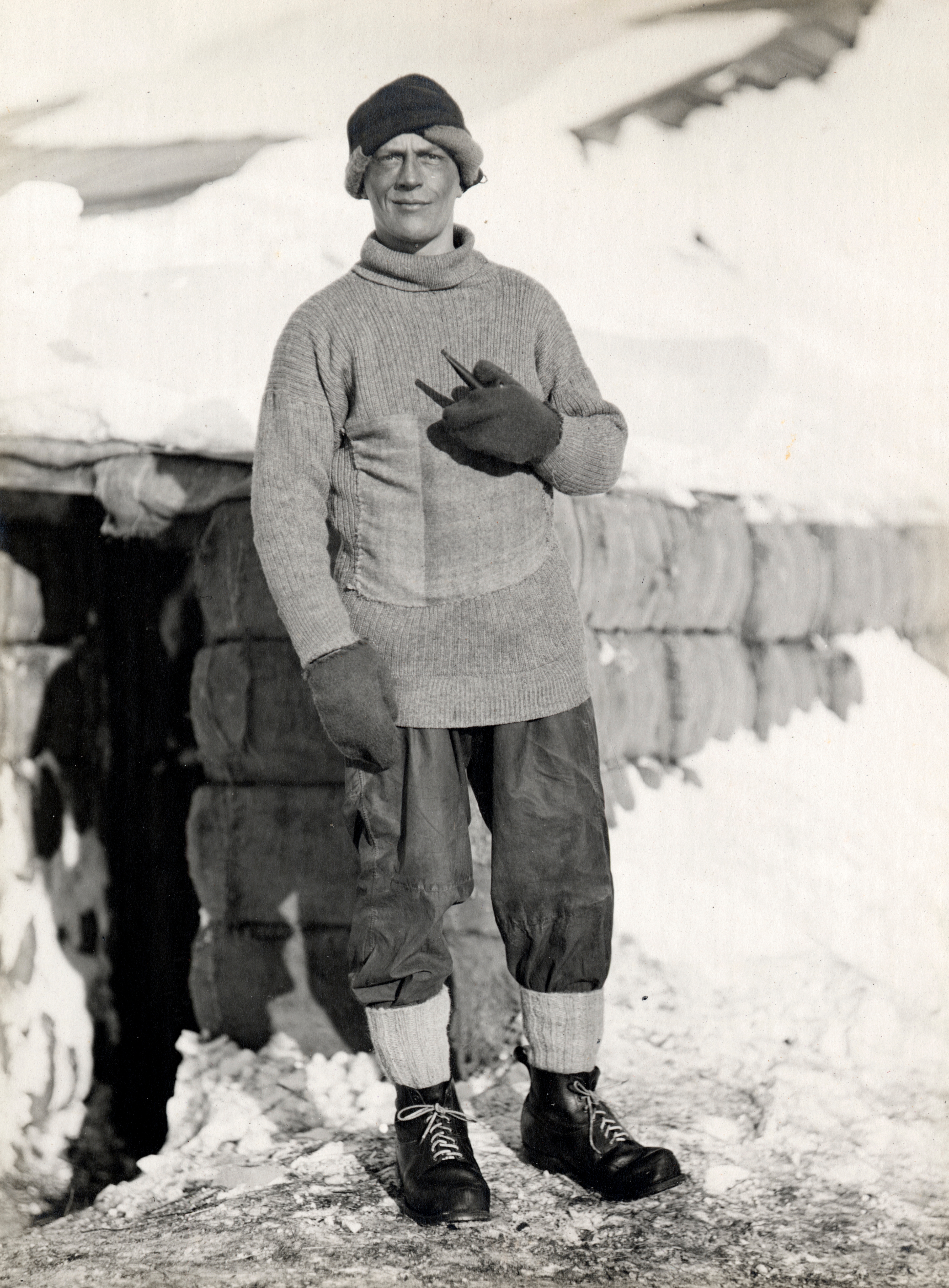 A idiosyncratic   astatine  a snowy determination  wearing a knit sweater, beanie, mittens, and trousers, holding a pipe, stands extracurricular  a log structure