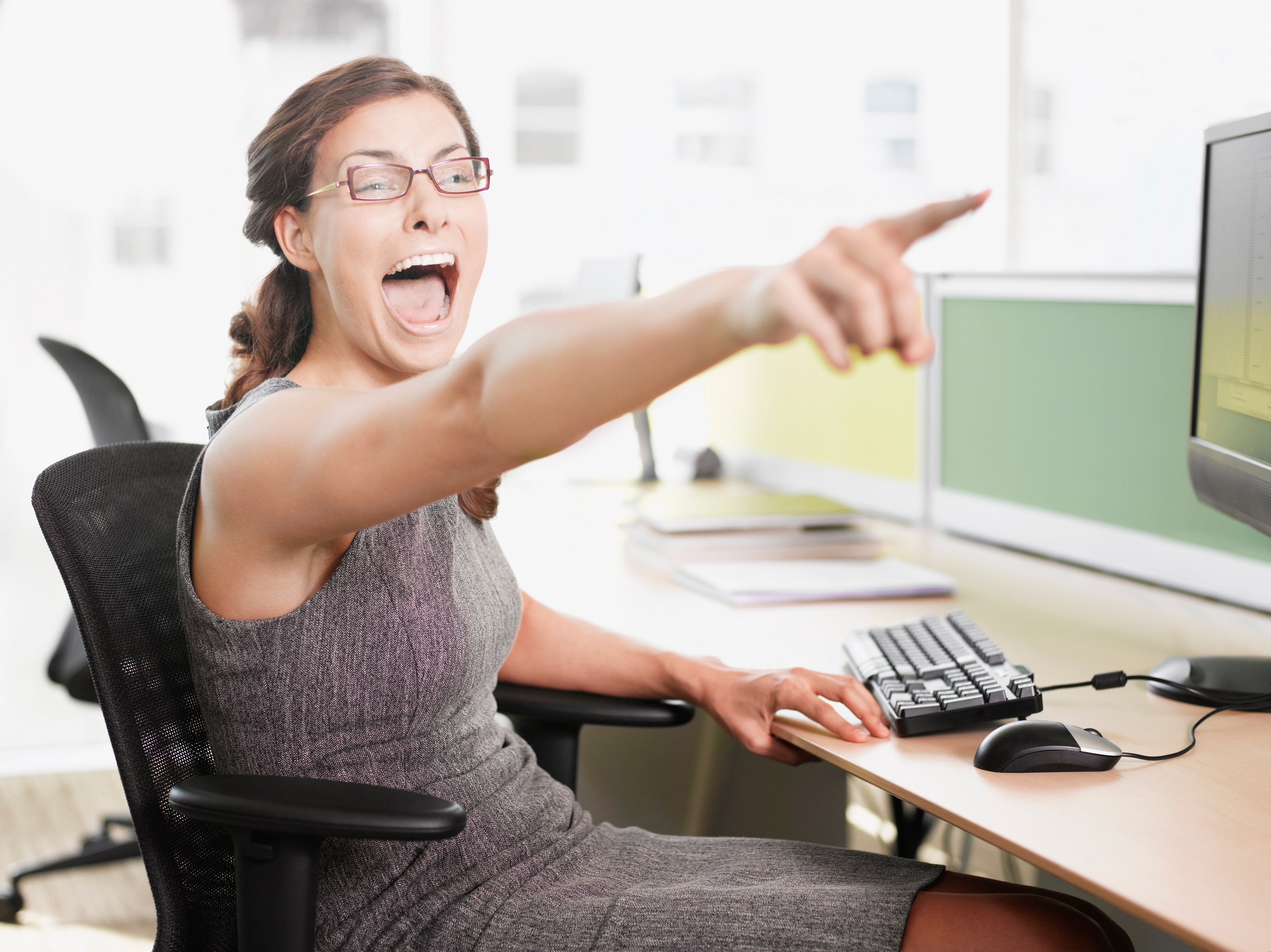 Person in office attire laughing and enthusiastically pointing at a computer screen