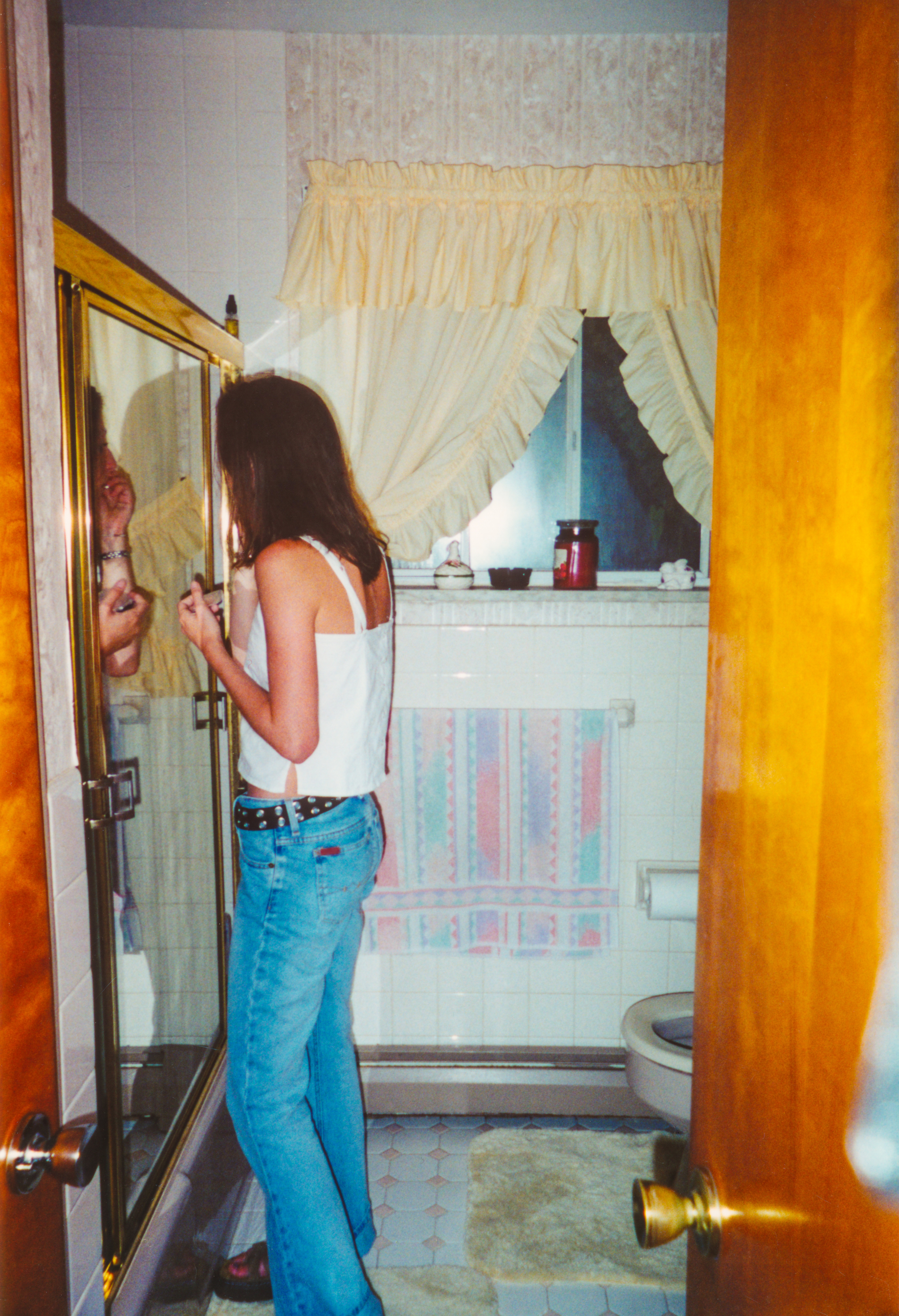 A pistillate successful a casual achromatic vessel apical and jeans stands successful a bath applying lipstick successful beforehand of a mirror