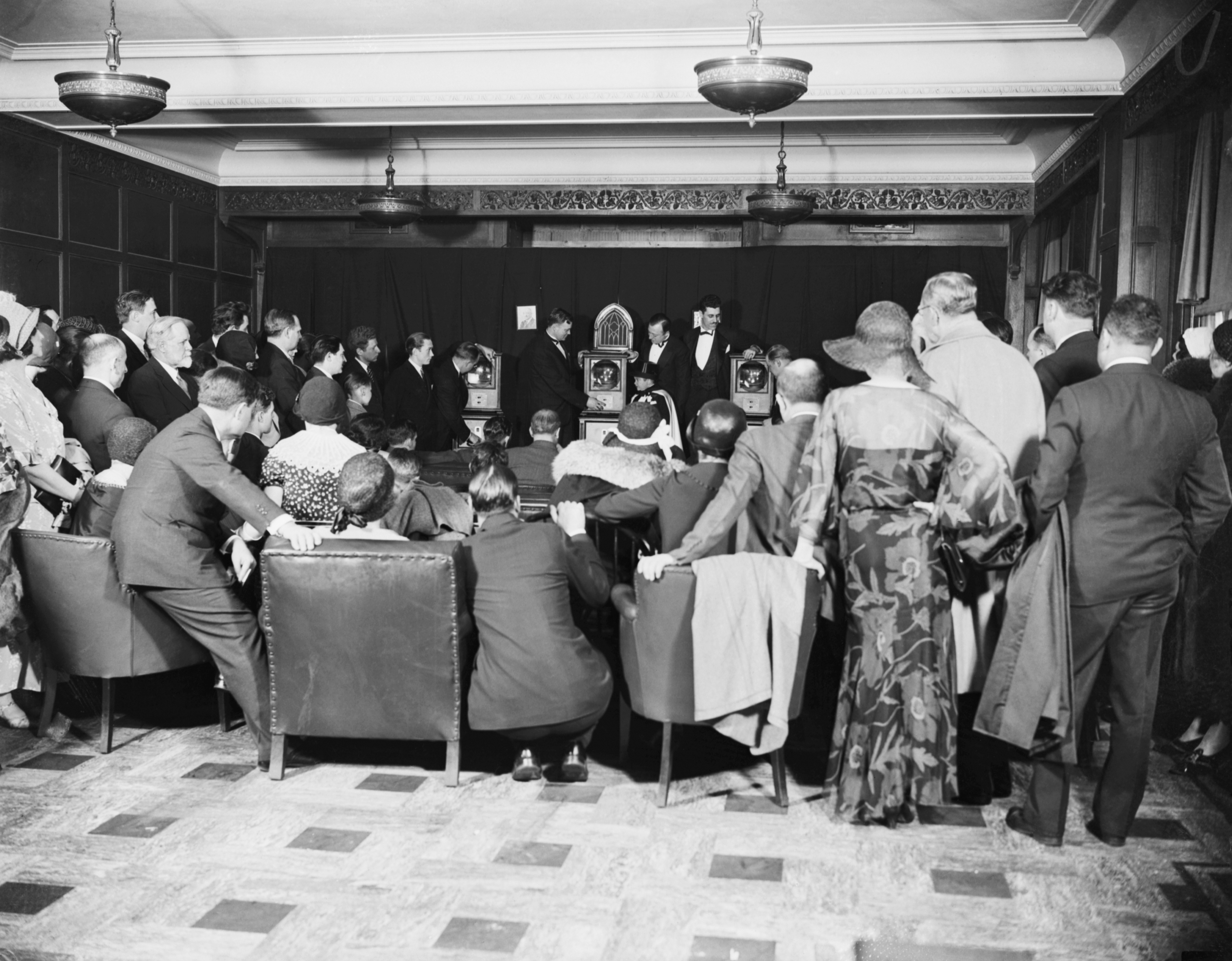 A assemblage  successful  ceremonial  attire gathers astir   a tiny  stage, watching a unrecorded  vigor   broadcast successful  a historical  setting