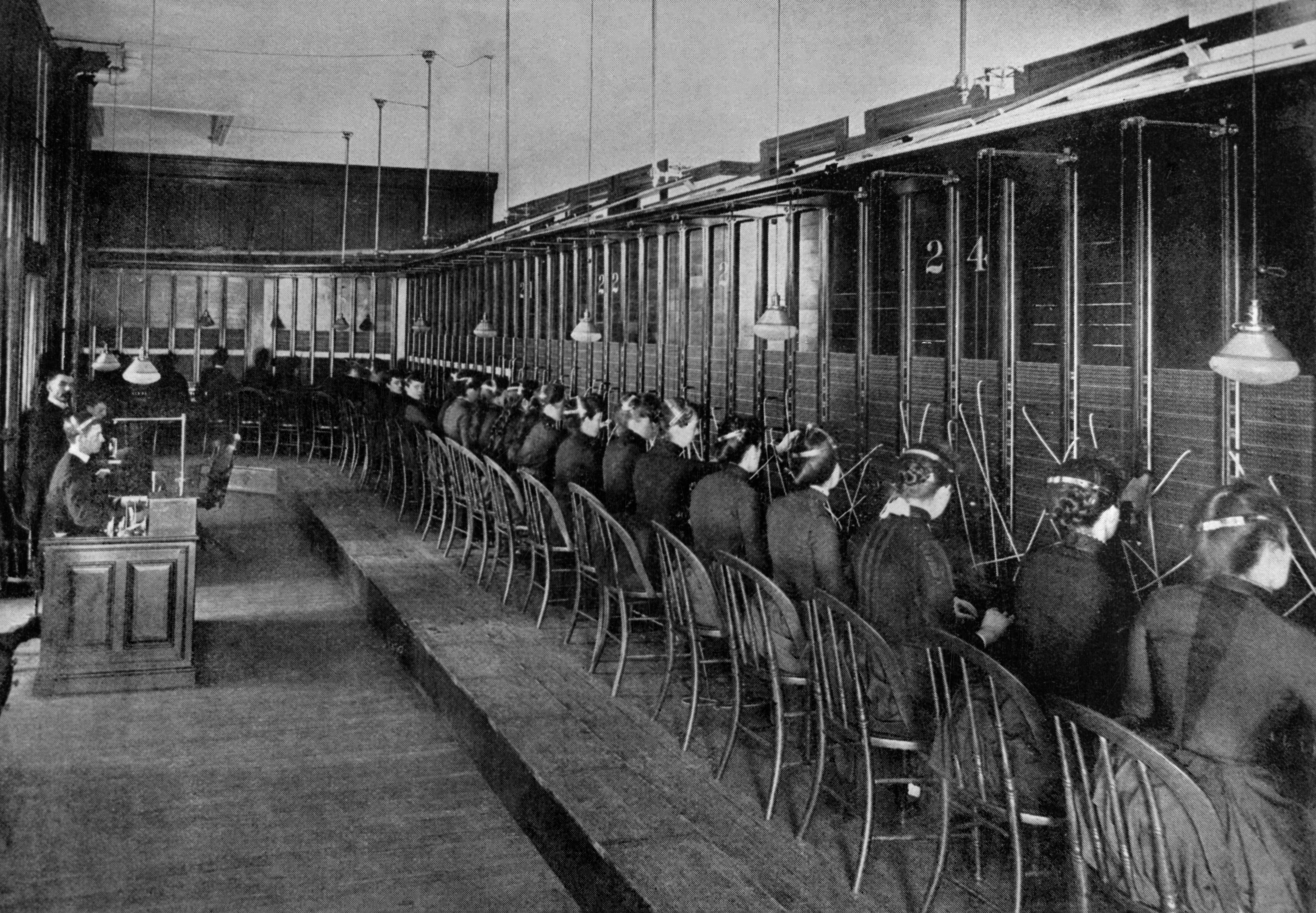 Historic photograph  of a agelong  enactment      of telephone   operators seated astatine  switchboards, managing calls successful  an aboriginal  20th-century speech   room
