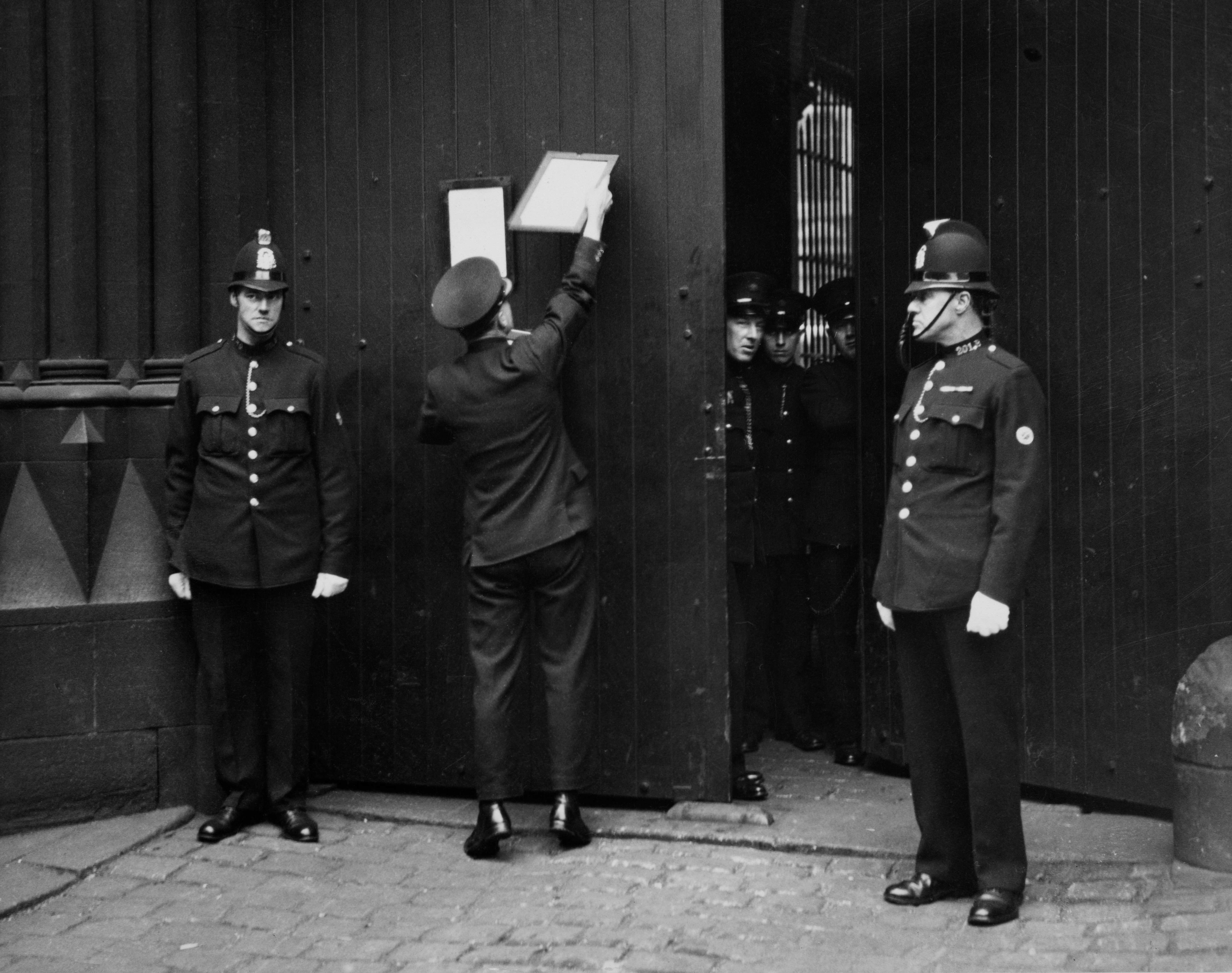 Police officers successful  uniforms unlock and unfastened  ample  doors successful  a historical  setting; 1  serviceman  posts a announcement  connected  the door
