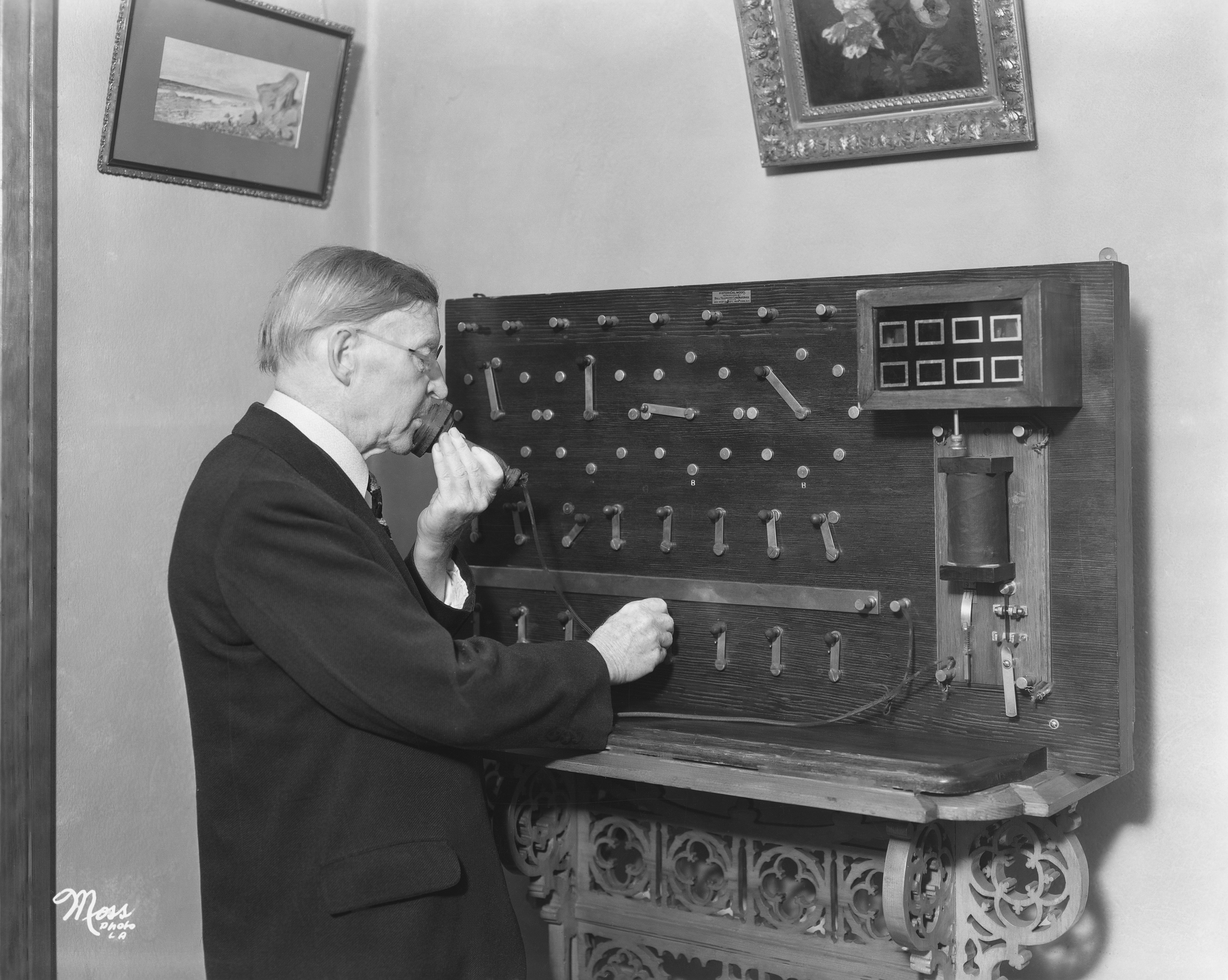 A antheral   operates an aboriginal  20th-century telephone   switchboard, placing a call. The country   features framed creation  and ornate furniture