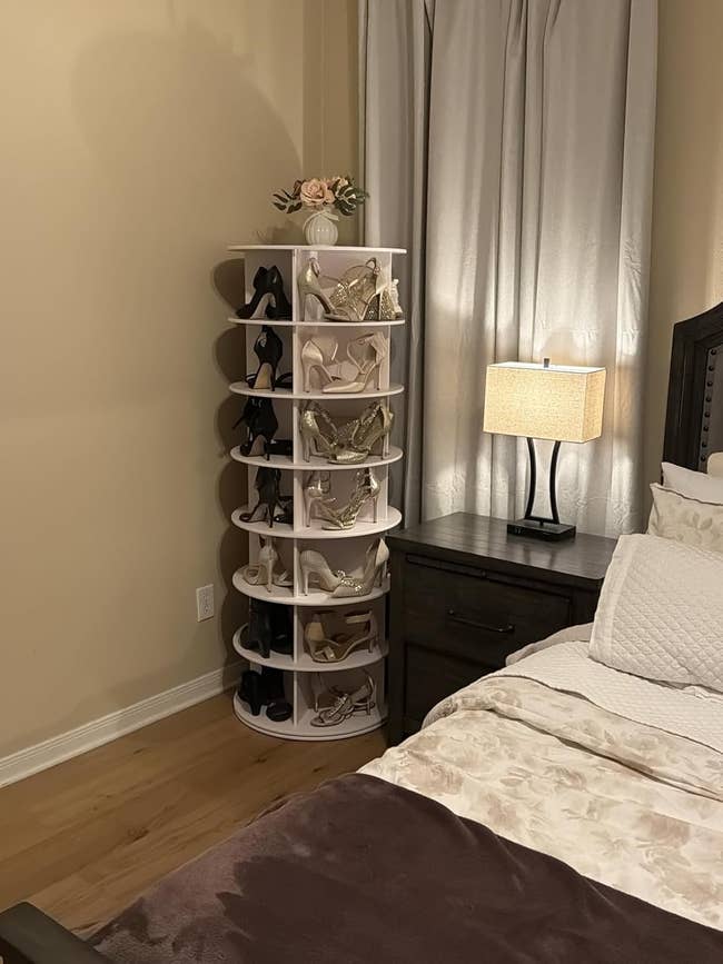 A rotating footwear rack filled with elegant precocious heels stands beside a furniture with a nightstand and lamp, suggesting chamber retention solutions