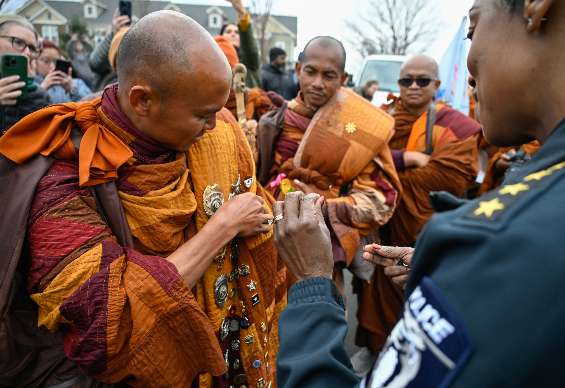 Biksu Buddha yang mengenakan jubah tradisional berinteraksi dengan petugas polisi selama acara publik, dikelilingi oleh penonton