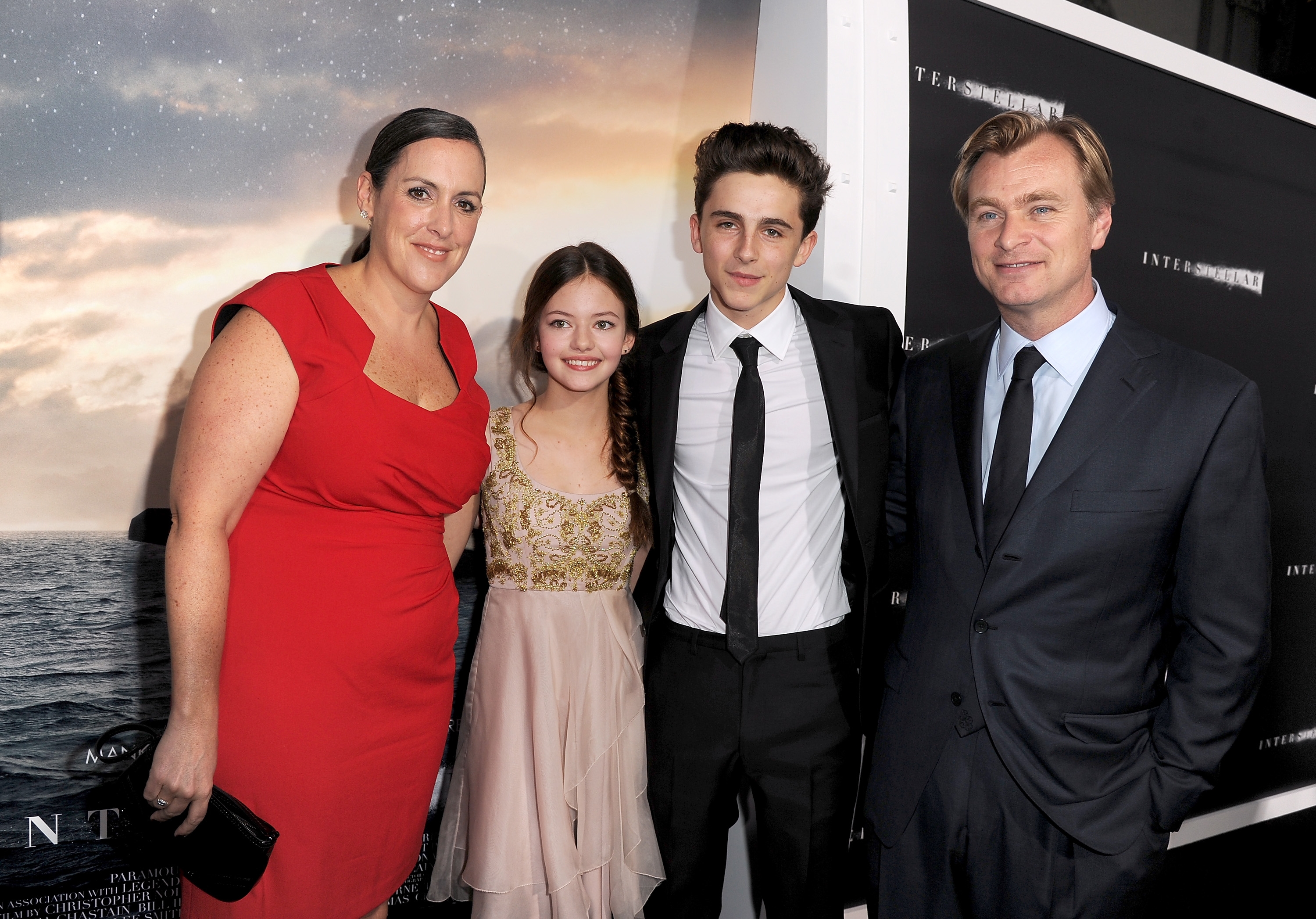 Group of 4  radical   astatine  a movie  event; 2  successful  ceremonial  suits, 1  successful  a reddish  dress, and different  successful  a gold-accented, sleeveless dress