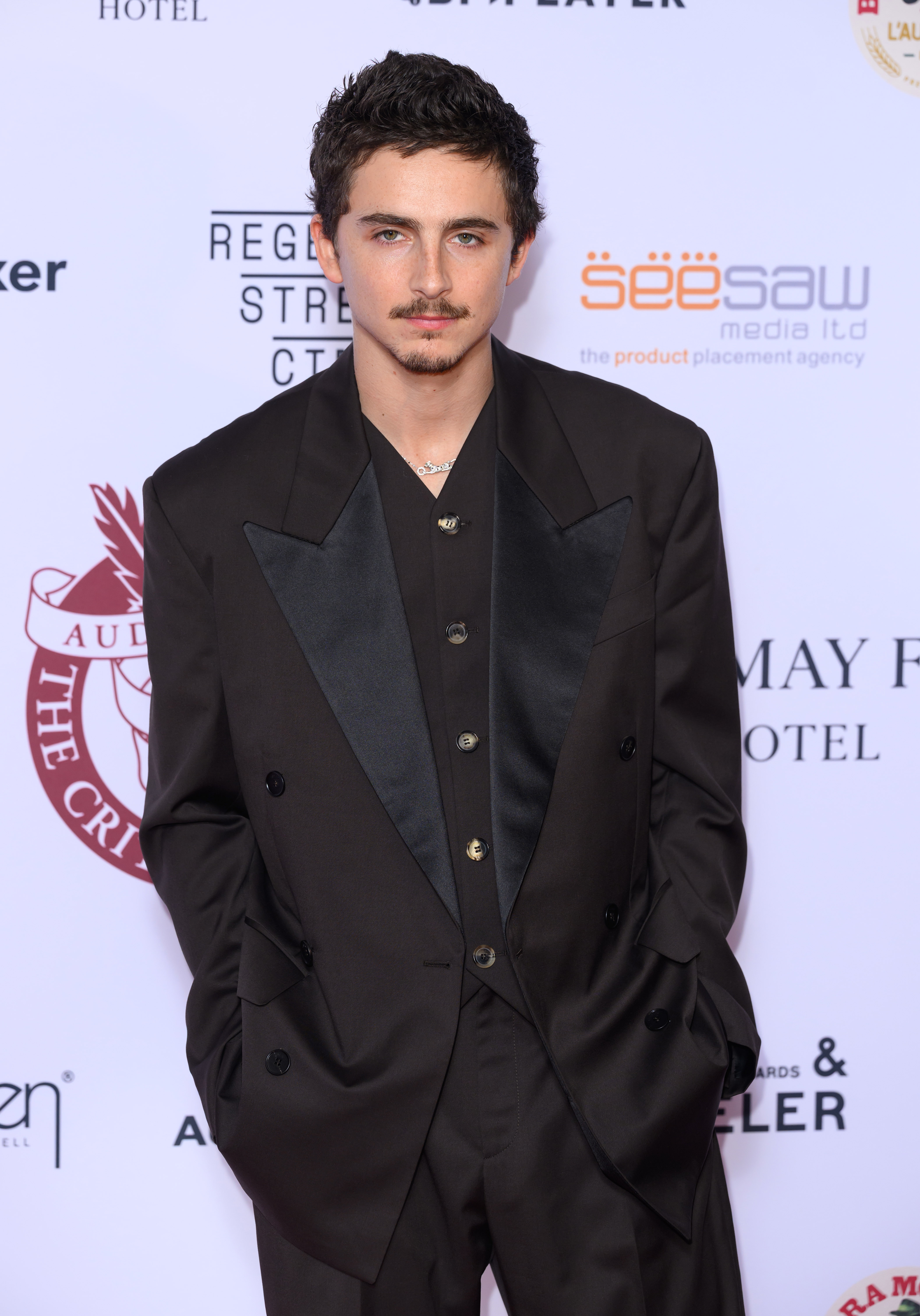 A idiosyncratic   successful  a stylish acheronian  suit   poses connected  a reddish  carpet, showcasing a relaxed yet elegant look   astatine  a personage  event