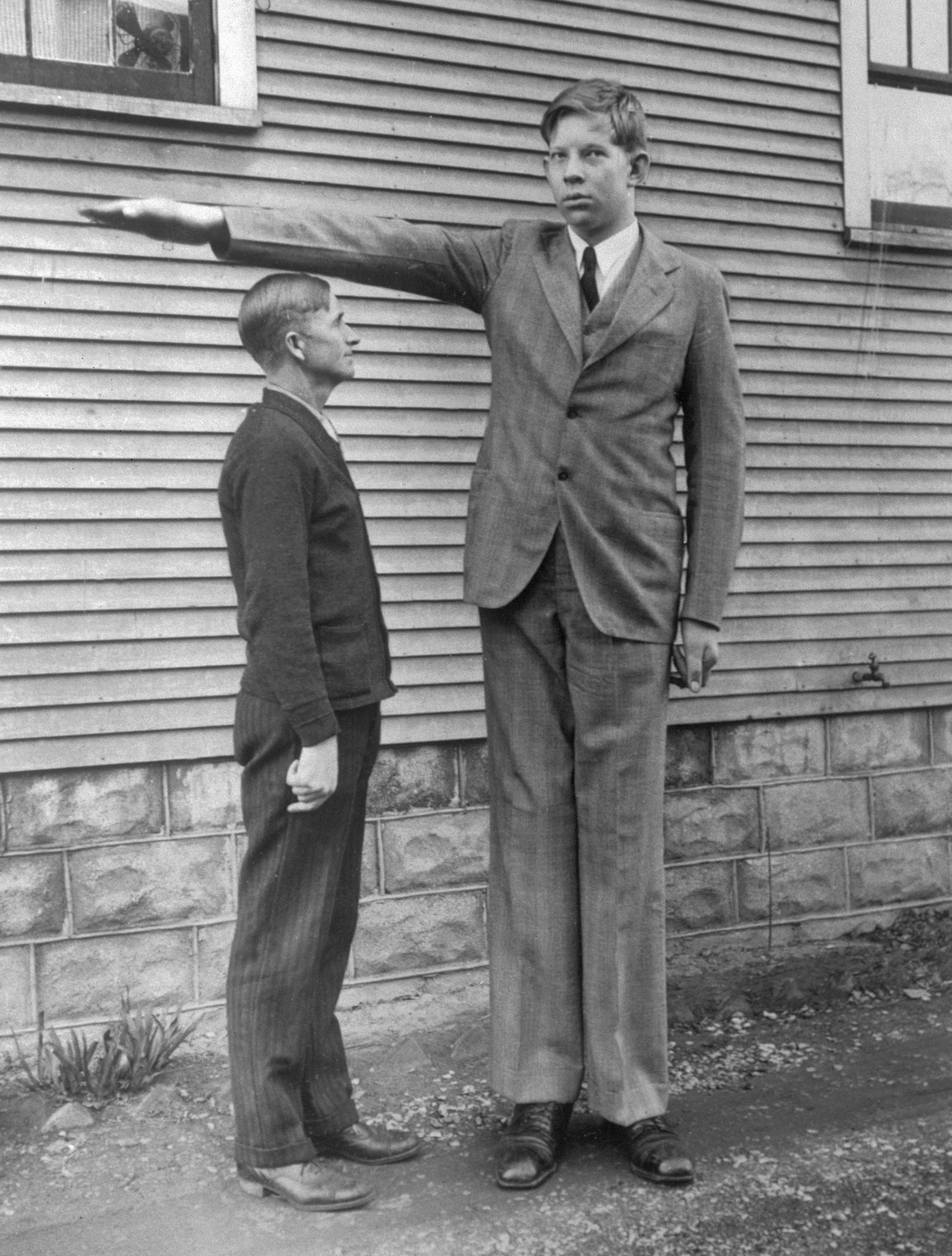 Two men basal   outside. A precise  gangly  antheral   successful  a suit   has 1  limb  extended horizontally implicit    the caput  of a shorter antheral   lasting  beside him