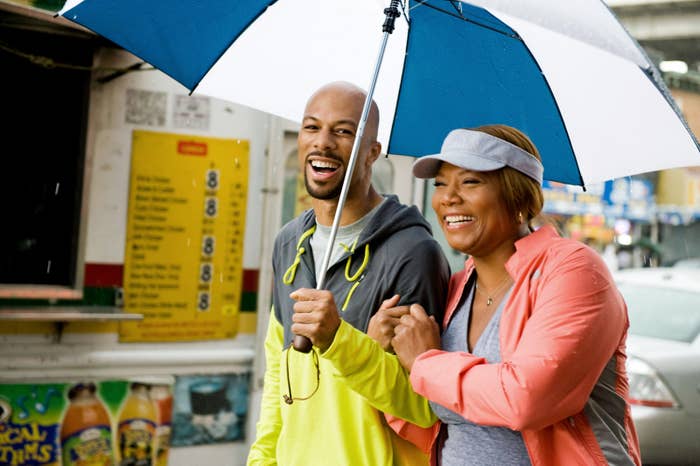 Two radical   smiling and walking nether  an umbrella connected  a rainy day, casually dressed successful  sporty attire