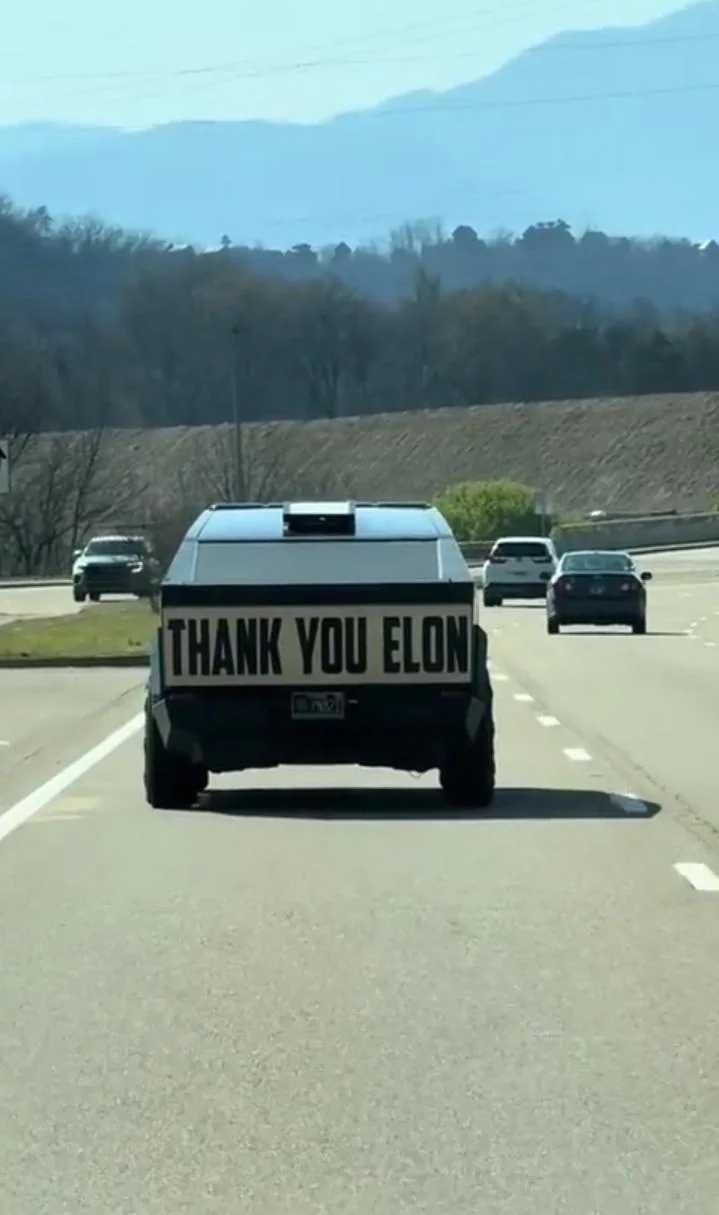 A conveyance  connected  a road  has a motion   speechmaking  "THANK YOU ELON" displayed connected  its rear