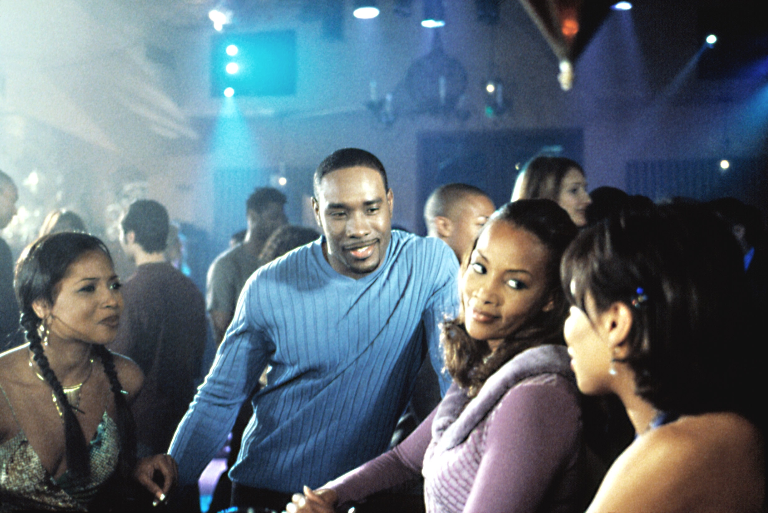 A radical of radical socializing astatine a lively indoor event, casually dressed. The ambiance is vibrant with a assemblage successful the background