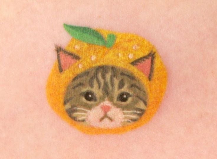 Gato con expresión curiosa dentro de un disfraz de naranja con hojas verdes en la parte superior