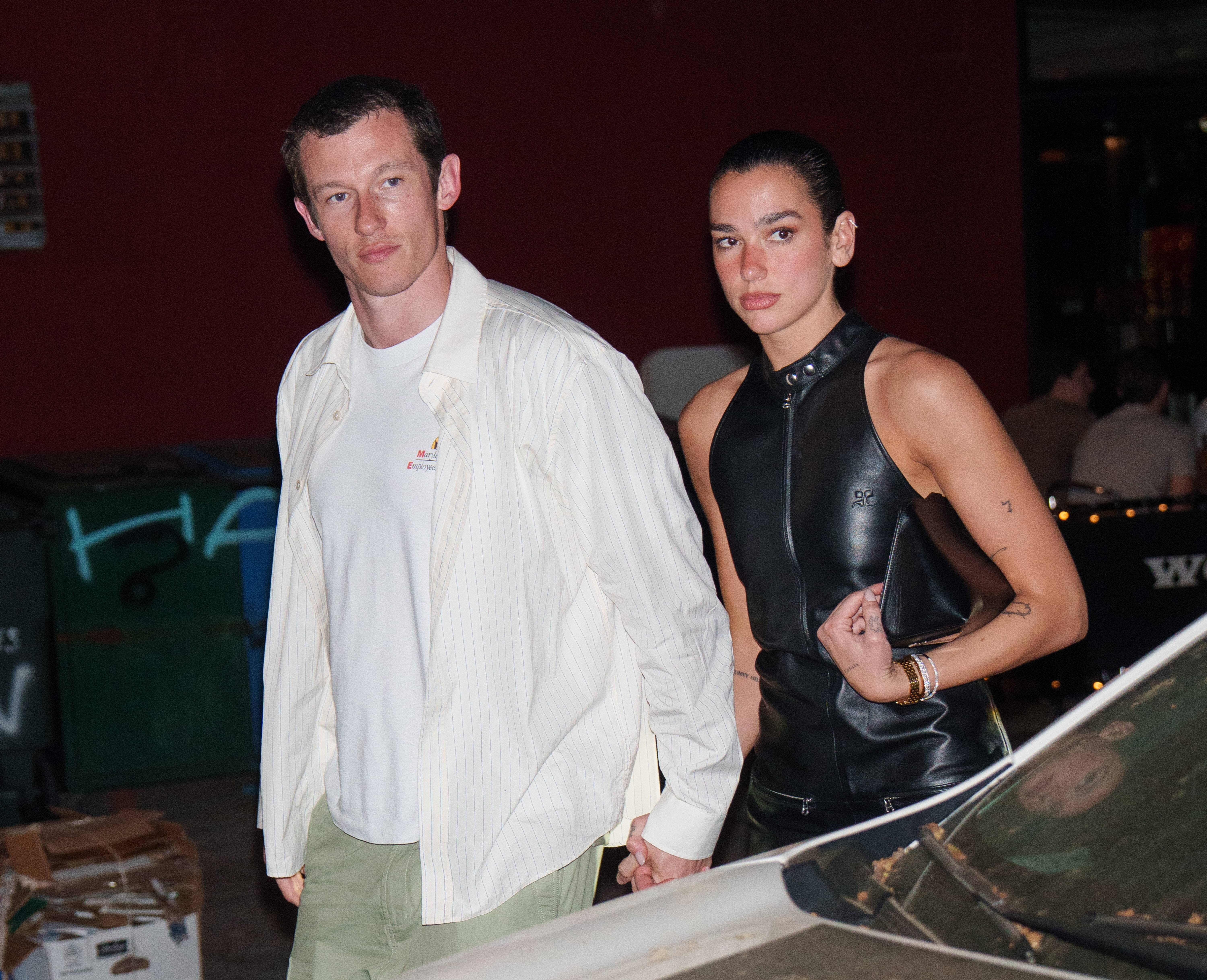 Callum Turner and Dua Lipa walking outside, holding hands