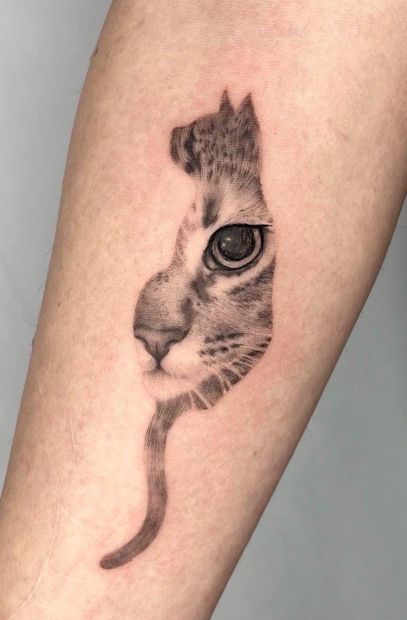 Tatuaje de un gato que combina el contorno de su cuerpo con su rostro detallado, en el antebrazo de una persona