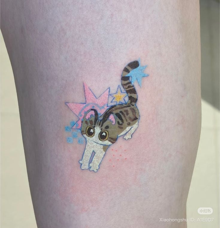 Tatuaje de gato animado con ojos grandes y diseño de estrellas azules y rosas