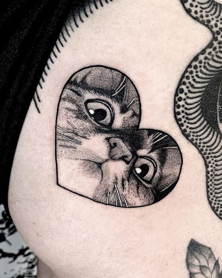 Tatuaje de un gato enmarcado dentro de un corazón en el brazo de una persona