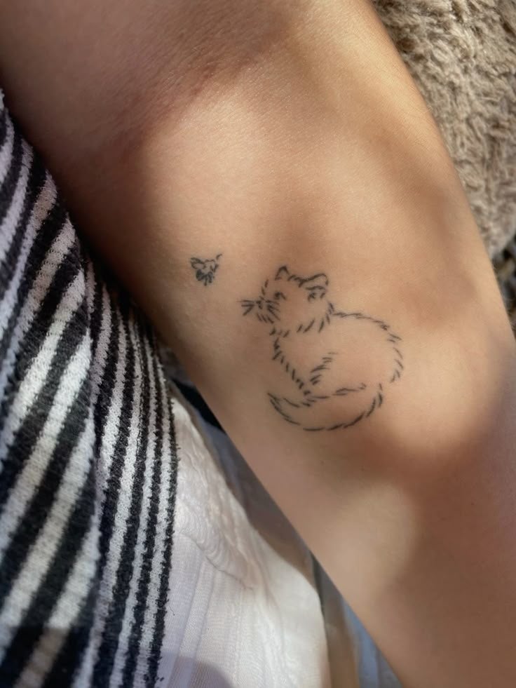 Tatuaje en el brazo de un gato mirando una mariposa pequeña