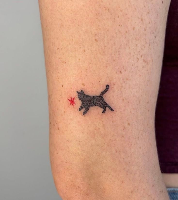 Tatuaje en el brazo de un gato negro mirando una pequeña estrella roja