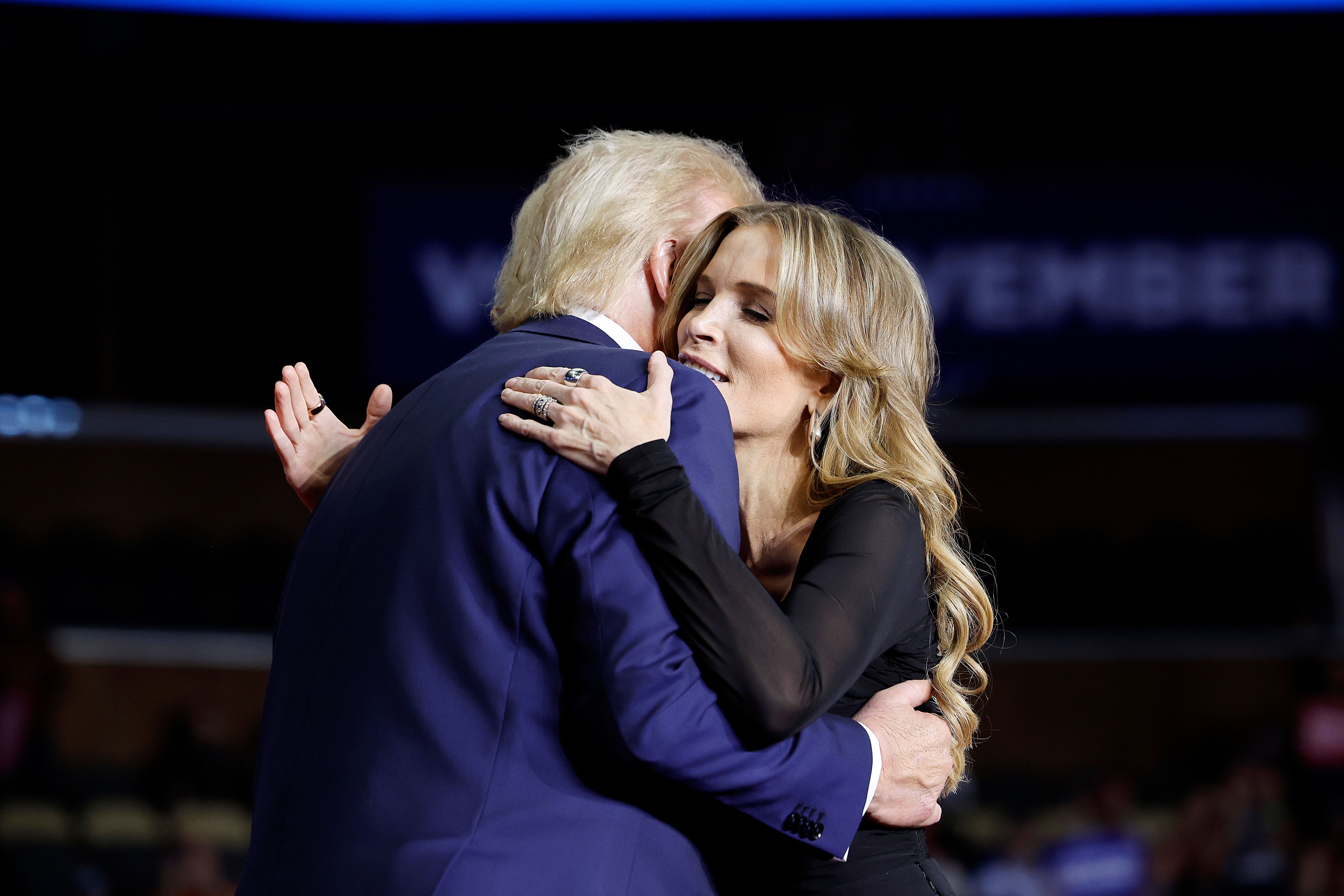 Two radical   embracing warmly connected  a signifier    indoors, with a blurred inheritance  featuring ample  substance   and an audience