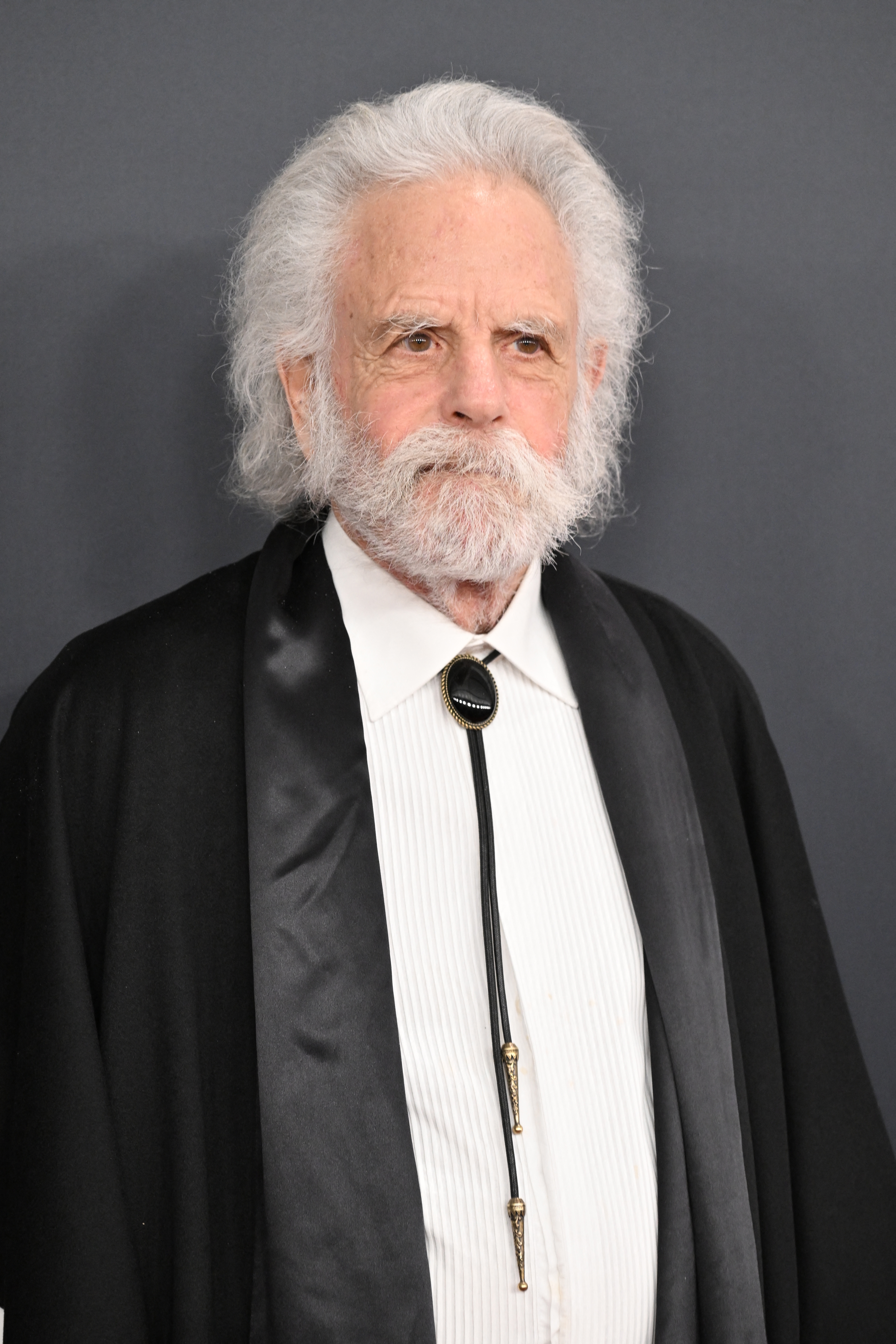 En eldre mann med hvitt hår og skjegg bærer en smoking med et slips på en formell begivenhet