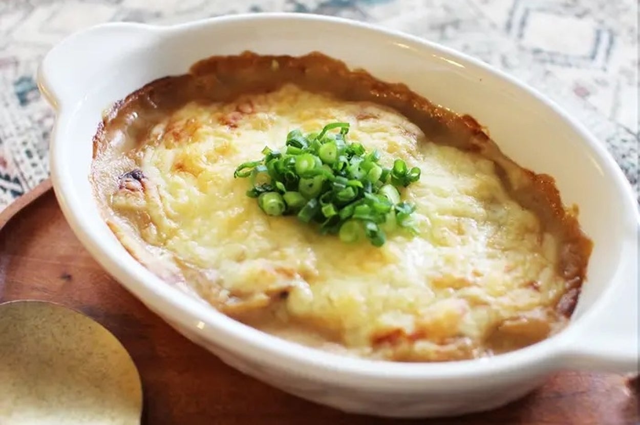 グラタン料理の上にネギが飾られているオーブン皿、隣にスプーンが置かれている。