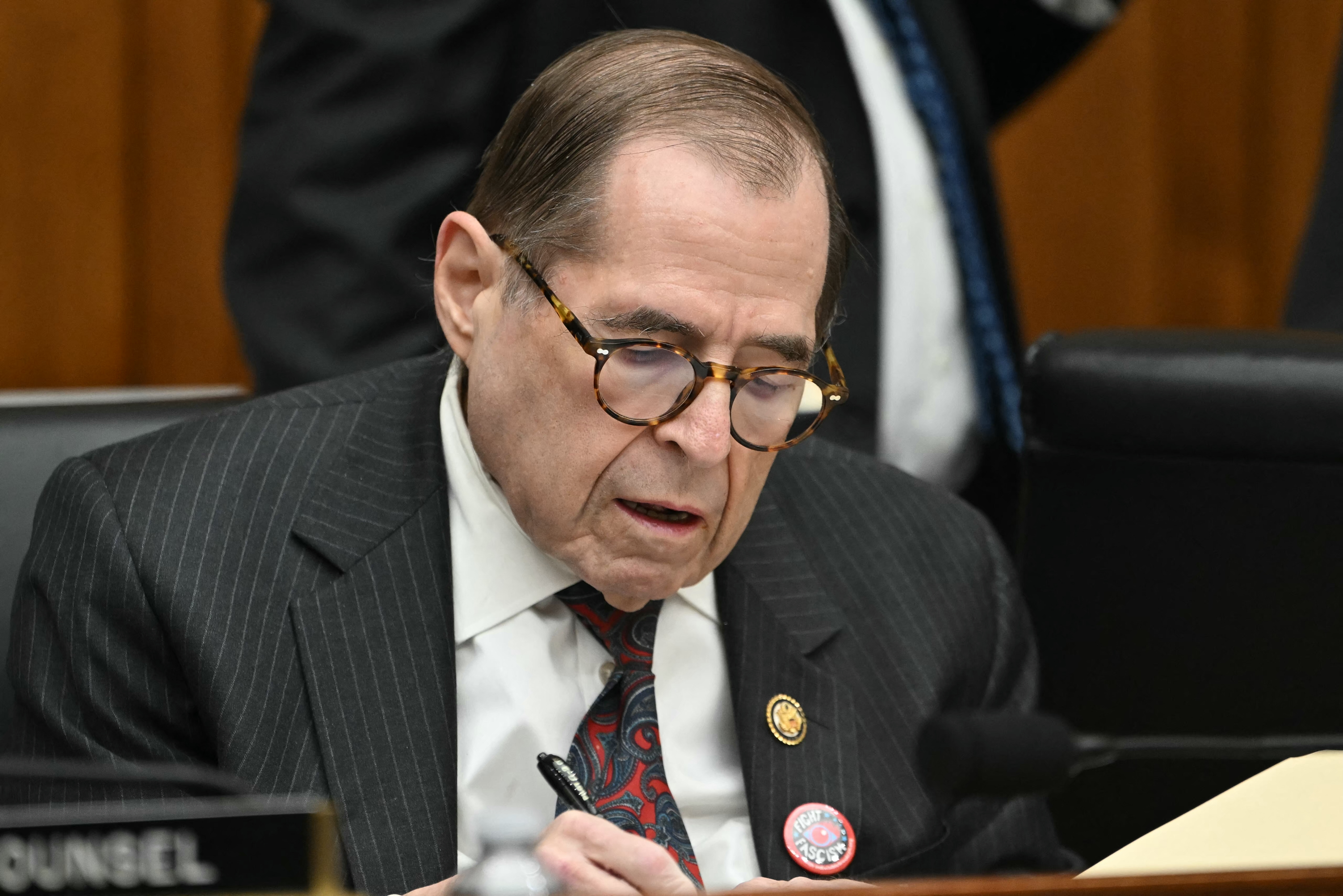 A idiosyncratic   successful  a pinstripe suit   with a badge, speechmaking  and writing, seated astatine  a array  during a ceremonial  lawsuit   oregon  meeting