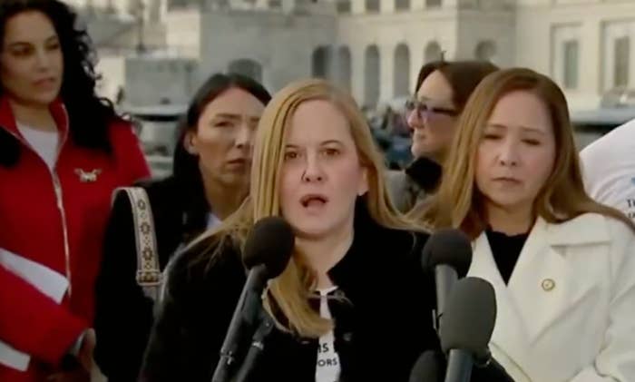 A radical  of women talk  astatine  an outdoor property   event. The pistillate   astatine  the halfway  wears a achromatic  outfit and speaks into aggregate  microphones