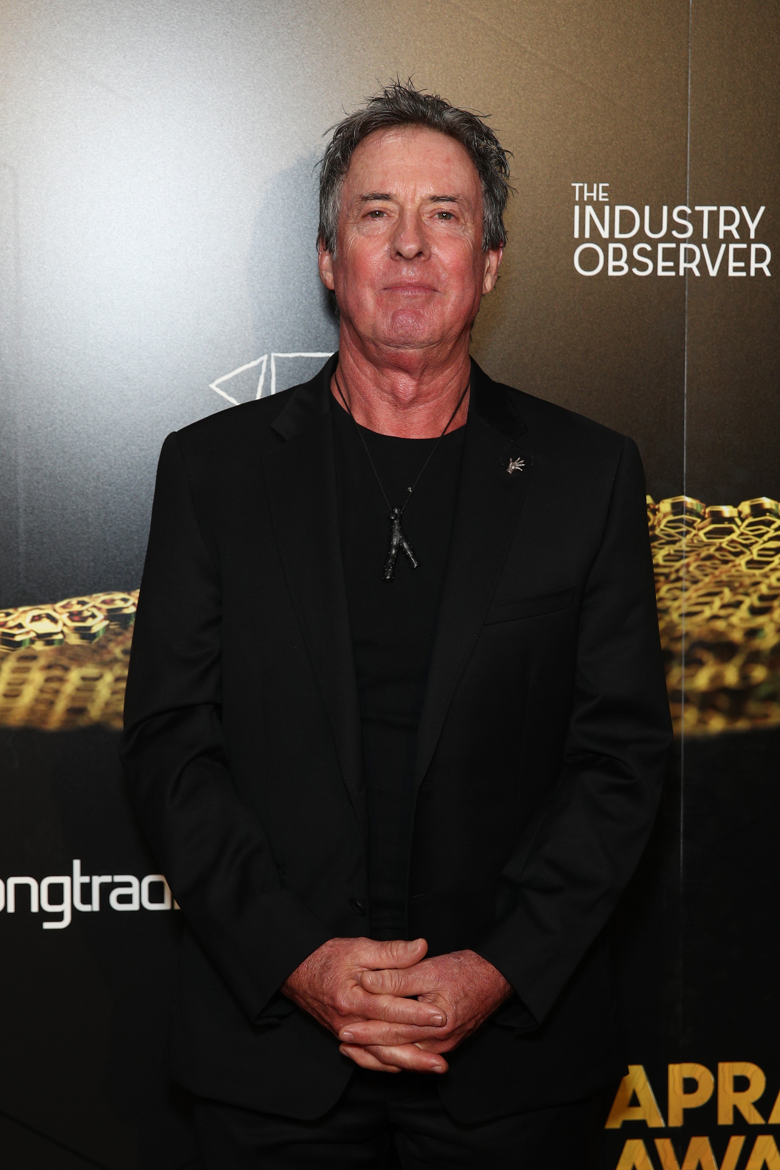 Person i svart dress og skjorte på et arrangement. Nøytralt bakteppe med eventlogo