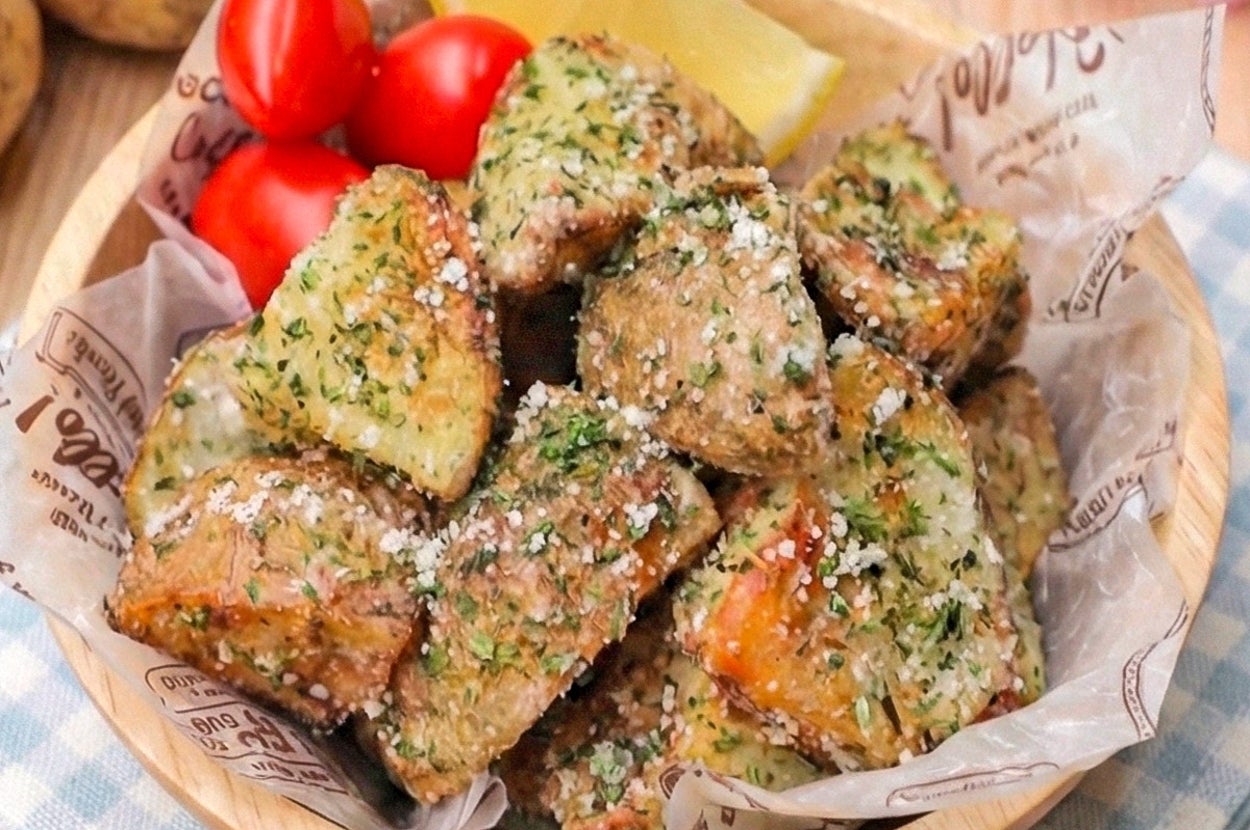 木製ボウルにハーブとチーズがかかったローストポテトとミニトマト、レモン。クラフト紙が敷かれている。