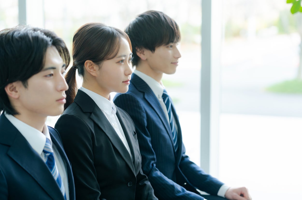 3人のビジネスパーソンが横に並んで座り、前を見つめている。スーツ姿で、会議かプレゼンテーションに参加しているよう。