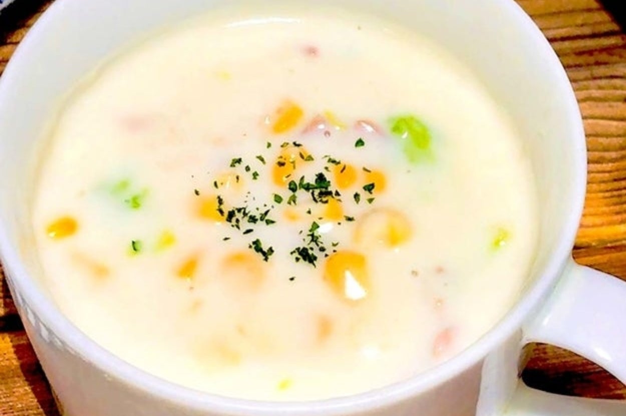 クリーミーなスープの入った白いカップ。上にはパセリのトッピングが見え、スプーンが横に置かれています。