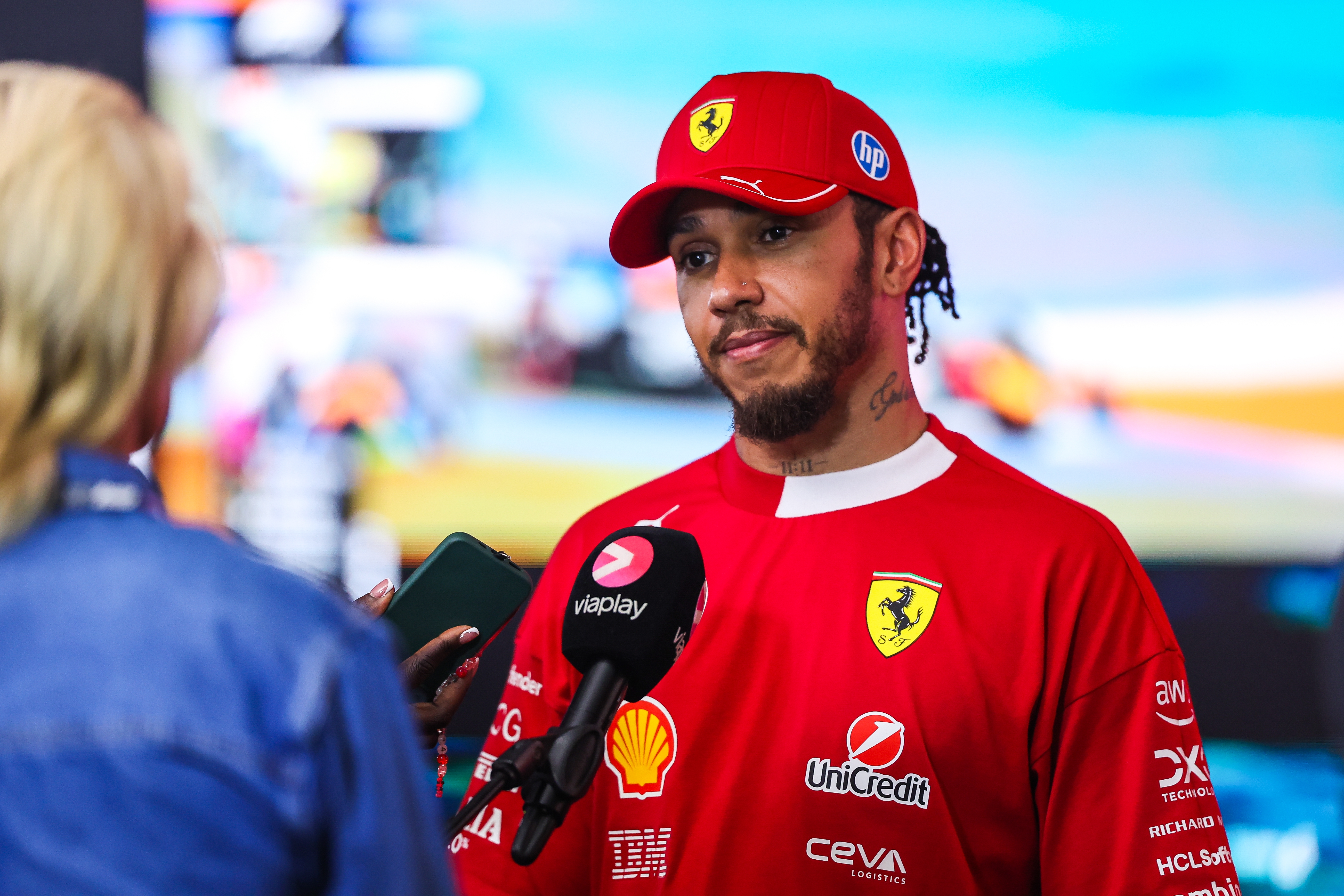 Race car   operator  successful  a reddish  squad  suit   and headdress  with sponsor logos speaks to a newsman  holding microphones