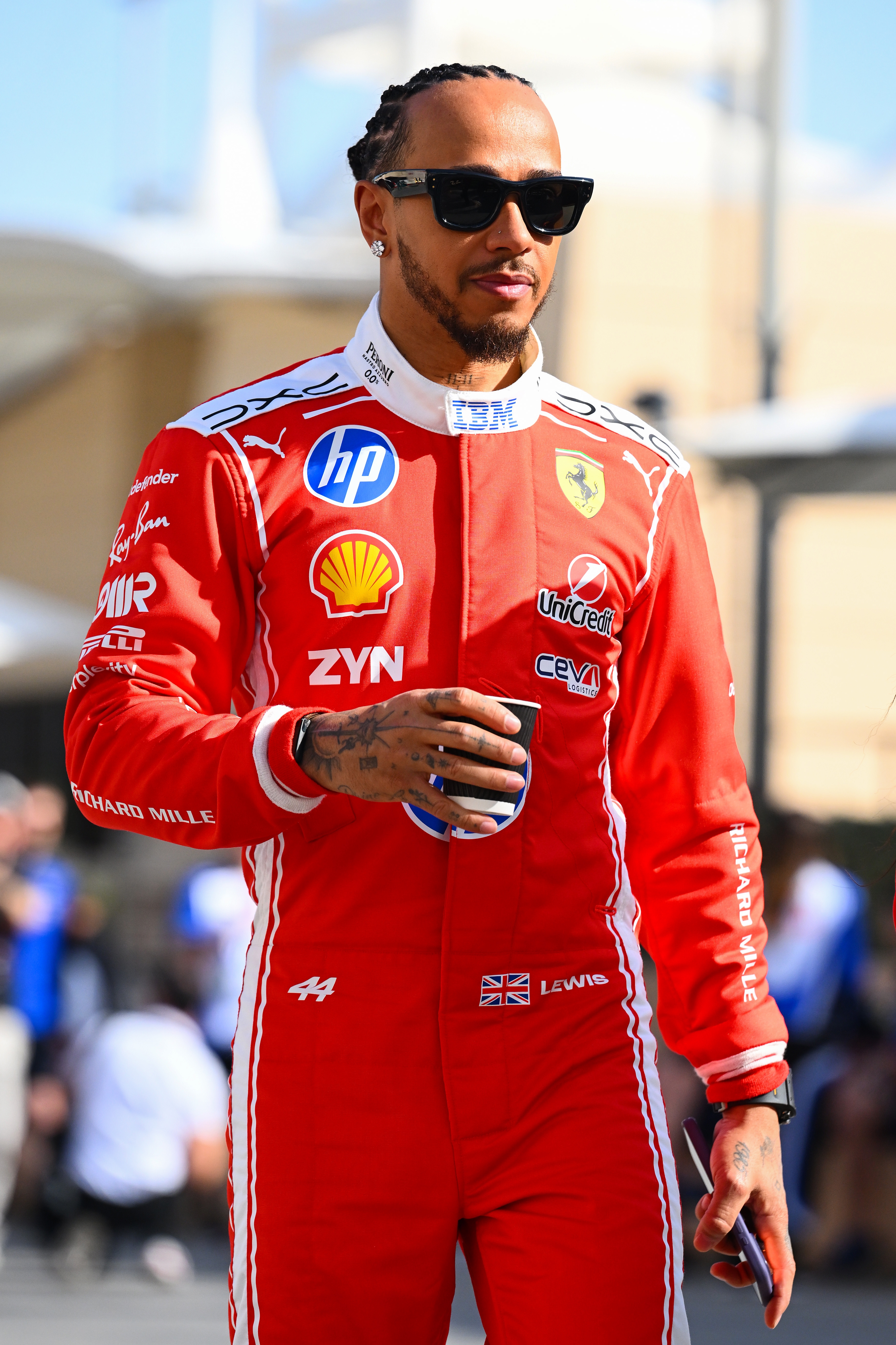 Person successful  a racing suit   with sponsor logos, wearing sunglasses and holding a drink, walking outside