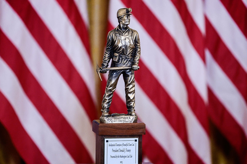 Statue of a ember miner with an ax connected a pedestal, acceptable against a backdrop of U.S. flags