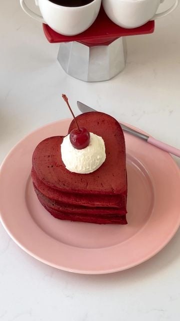 Torre de panqueques en forma de corazón con crema y una cereza encima, en un plato redondo