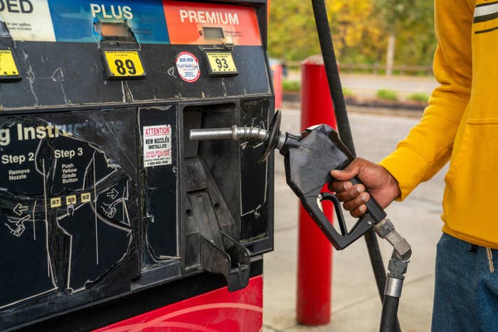 Person successful  a yellowish  overgarment   refuels a conveyance  astatine  a state  station, holding a state  pump nozzle adjacent   an unleaded pump