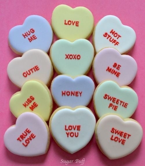 Doce galletas en forma de corazón con mensajes como "LOVE", "HUG ME", "BE MINE", y "KISS ME"