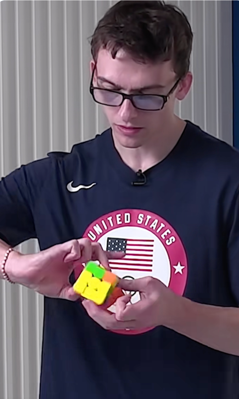 Person intently solves a Rubik's Cube, wearing a t-shirt with "United States" and an emblem