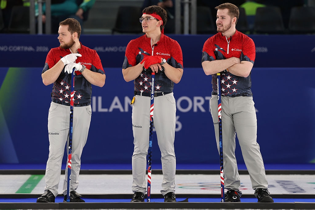 Three men successful  matching curling uniforms basal   holding brooms, apt  astatine  a sports event. They look   focused and attentive